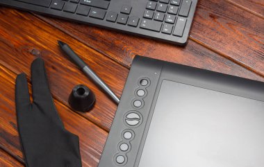 Grafik tablet, dijital tablet ve özel kalem, ahşap bir masada eldiven ve klavye. Yakından, üstten, düz. Serbest çalışan, tasarımcı, çizer. Teknoloji, uzaktan kumanda, dış kaynak kullanımı. konsept