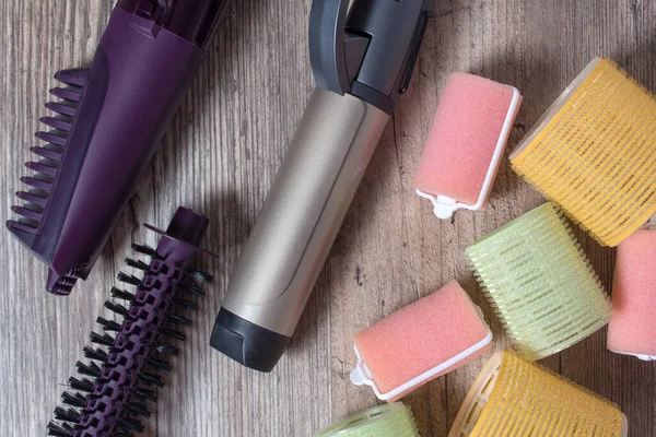 Ceramic Curling iron, hair brush and velcro curlers on a wooden background. Hot styling, boar bristles, hair care. Beauty salon. Curl, wave, volume. Beauty, fashion, style. Hairdresser. Hair roller