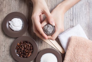 Genç bir kadın elinde bir kavanoz ev yapımı kahve fırçası tutuyor. SPA, güzellik. Fırça, kahve çekirdeği, şeker, krema yapmak için gerekli malzemeler. Cilt bakımı. Nemlendirici, deri yüzücü, soyucu. Ev Kozmetikleri, Eko