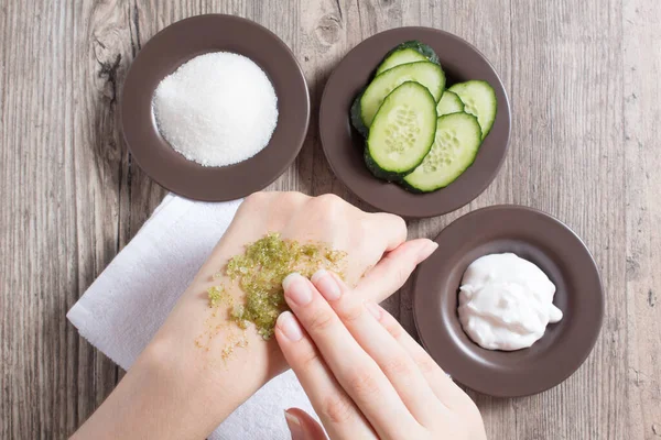 Skin care at home. A woman applies a natural homemade scrub to her hand. Ingredients for making the scrub, salt, sugar, cucumber, cream. Moisturizing, peeling, exfoliation, SPA, beauty salon. Eco
