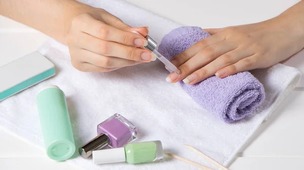 Manicure. A woman applies a moisturizer to the cuticle. Manicure tools, nail polishes, oil. Home nail care, SPA, beauty. Long natural nails. Beauty salon.