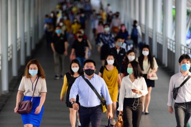 Trafiğin yoğun olduğu saatlerde metro istasyonunda yürüyen cerrahi maske takan insanlar.