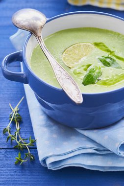 Mavi arka planda yeşil yapraklı brokoli kremalı çorba.