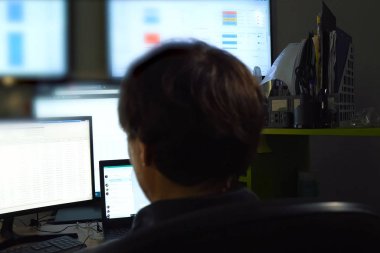 Hacker monitörün arkasında oturuyor ve çalışıyor. Bilgisayar teknisyeni ve programcının işi..