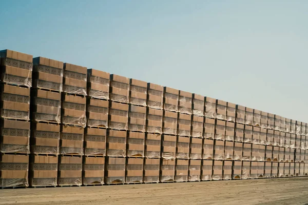 Bricks are stored in an open-air warehouse. Red brick in pallets.