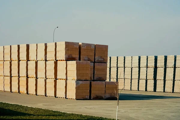 Bricks are stored in an open-air warehouse. Red brick in pallets.