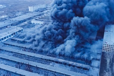 Fabrikada büyük bir yangın. Binalardan siyah dumanlar yükseliyor.