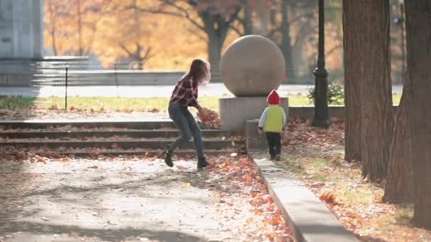 Giovane madre divertirsi con il figlio bambino nel parco autunnale, giocando con le foglie — Video Stock