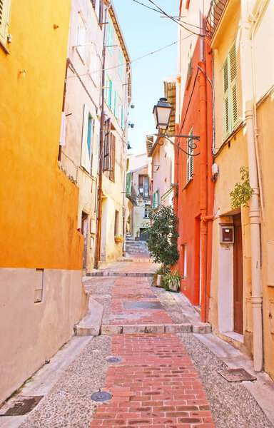 The narrow hilly street with the colorful houses and old-fashioned lanterns, Menton, France.