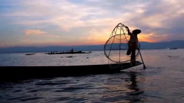 Günbatımı gökyüzü ve bacak kürek balıkçı, Kano'nın yay üzerinde duran ve geleneksel hileler ile net ve kürek, Inle Gölü, Myanmar gösteren karanlık siluet.