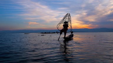 Bir bacak Inle Gölü, Myanmar akşam karanlık sular arasında kürek çekmeye alışılmadık tekniği gösteren Kano, Birmanya balıkçı karanlık siluet.