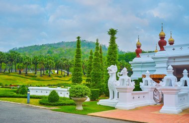 The scenic topiary thuja trees and plants in pots at the white statue of Singha lion and garden vases, Rajapruek park, Chiang Mai, Thailand clipart