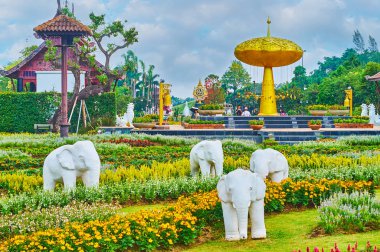 CHIANG MAI, THAILAND - MAY 7, 2019: The white elephants sculptural group in front of the symbol of Rajapruek park - the golden shower tree, on May 7 in Chiang Mai clipart