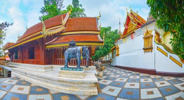 Panorama of Lanna style Viharas (shrines) of Wat Phra That Doi Suthep temple with gilt Naga serpents, pyathat roofs, carved patterns and bronze elephant statue on the foreground, Chiang Mai, Thailand clipart