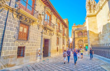 GRANADA, SPAIN - SEPTEMBER 27, 2019: Tourists walk in Calle Oficios (La Lonja square), lined with historic buildings of Capilla Real (Royal Chapel) and Palacio de la Madraza (Madrasah school), on September 27 in Granada