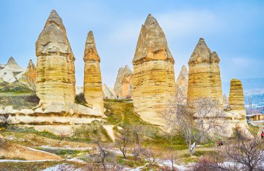Goreme Milli Parkı 'nın uzun parmak şeklinde oluşumları, meyve ağaçları ve karlı çimlerle çevrili, Kapadokya, Türkiye