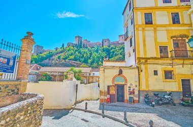 GRANADA, SPAIN - SEPTEMBER 25, 2019: Tiny Plazeta de la Concepcion square with medieval house of Teteria El Banuelo cafe and a view on Sabika hill, topped with Alhambra, on September 25 in Granada