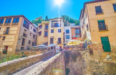 GRANADA, SPAIN - SEPTEMBER 25, 2019: The stone Puente Cabrera bridge leads to the old narrow streets at the foot of Sabika hill with old buildings, cafes, bars and other tourist spots, on September 25 in Granada