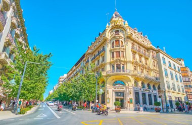 GRANADA, SPAIN - SEPTEMBER 25, 2019: The view on Calle Gran Via de Colon from the Plaza Isabel la Catolica square, overlooking historic mansions, lines of lush trees and fast traffic, on September 25 in Granada