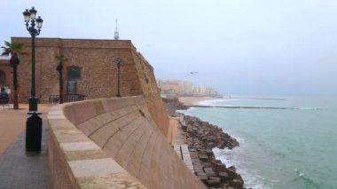 Atlantik Okyanusu kıyısında yağmurlu bir sabah Cadiz kalesinin Baluarte de San Roque (kalesi) manzaralı, sisli yağmurlu gökyüzü ve fırtınalı sular, İspanya