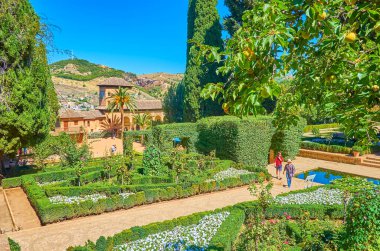 GRANADA, SPAIN - SEPTEMBER 25, 2019: The scenic Partal garden of Alhambra with topiary plants, colorful flowers in flower beds, pool and Partal palace on background, on September 25 in Granada clipart