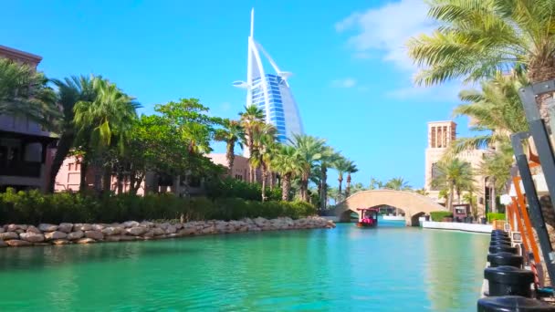 ドバイ アラブ首長国連邦 2020年3月4日 観光船は3月4日にドバイでヤシの木の後ろに見られる豪華なブルジュ アラブのホテルを眺めながら マディナ ジュメイラ複合体の狭い運河を通って浮かび上がります — ストック動画