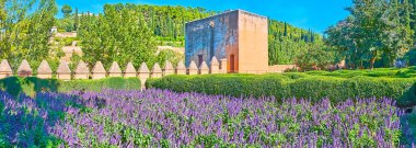 Surları olan Alhambra bahçesi panoraması, siperlerle kaplı, ortaçağ Yargıç Kulesi (Torre del Cadi, Mahkûm Kulesi) ve çiçek açan ultra mor salvia (adaçayı), Granada, İspanya