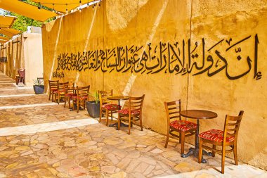 DUBAI, BAE - 2 Mart 2020 'de Dubai' de Al Fahidi ilçesinde Arap kaligrafisi ile dekore edilmiş, gölgeli kil duvardaki küçük kahve standı masaları