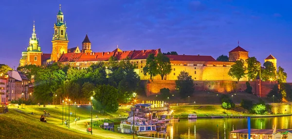 The amazing medieval Wawel Castle in evening lights and the youth relaxing on grass and walk along promenade, Krakow, Poland