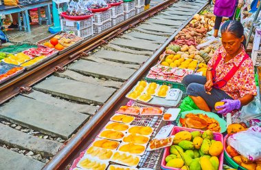 MAEKLONG, THAILAND - 13 Mayıs 2019: Maeklong Demiryolu Market meyve tezgahı tüccarı, 13 Mayıs 'ta Maeklong' da demiryolu kenarında oturan plastik konteynırlara papaya ve mango dilimleri paketliyor