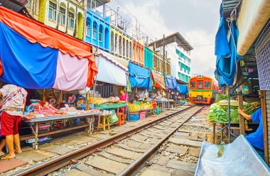 MAEKLONG, THAILAND - 13 Mayıs 2019: Tren, 13 Mayıs 'ta Maeklong Demiryolu Pazarı dar geçidi boyunca, taze sebze ve meyve tezgahları, küçük kafeler ve dükkanlarla dolu, yavaş yavaş ilerliyor.