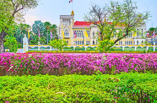 БАНГКОК, Таиланд - 13 мая 2019 года: Фасад дворца Тай-Кху-Фа Дома Правительства через пышные зеленые и бугенвиллийские цветы вокруг канала Клонг Прем Прачакон, 13 мая в Бангкоке
