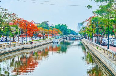 BANGKOK, THAILAND - 13 Mayıs 2019: 13 Mayıs 'ta Bangkok' ta Khlong Phadung Krung Kanalı 'nın ayna yüzeyi taş bankaları, çiçek açan ateş ağaçları ve klasik yaya köprüsünü yansıtıyor.