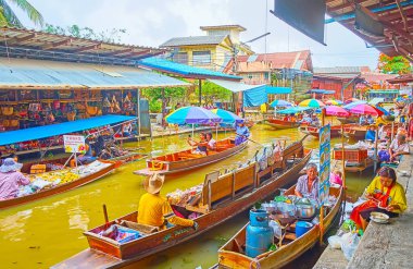 DAMNOEN SADUAK, THAILAND - MAY 13, 2019:  The numerous moored sampan food boats attract tourists to buy the lunch or some fruits and eat on the bank of Damnoen Saduak floating market with a view on khlong, on May 13 in Damnoen Saduak clipart