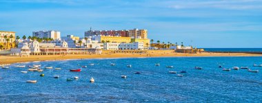 La Caleta sahil şeridi kıyı kafeleri, güneşlikler, dinlenme alanı ve limana demirlemiş küçük balıkçı tekneleri, Cadiz, İspanya