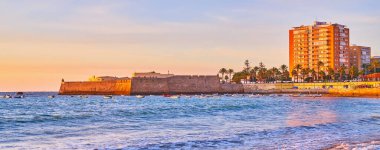 Santa Catalina ortaçağ şatosu, dalgalarda sallanan küçük balıkçı tekneleri ve mor gökyüzü, Cadiz, İspanya