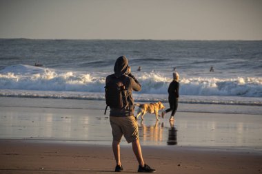 Sahilde sörfçülerin fotoğrafını çeken bir fotoğrafçı.