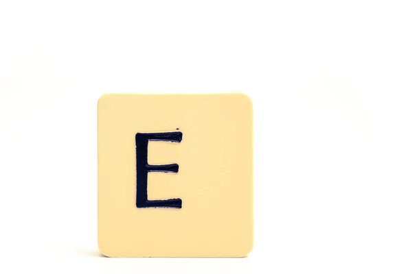 Mörk bokstav E på en blekt gul fyrkantig block isolerad på vit ba — Stockfoto