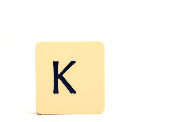 Dark letter K on a pale yellow square block isolated on white ba — Stock Photo, Image