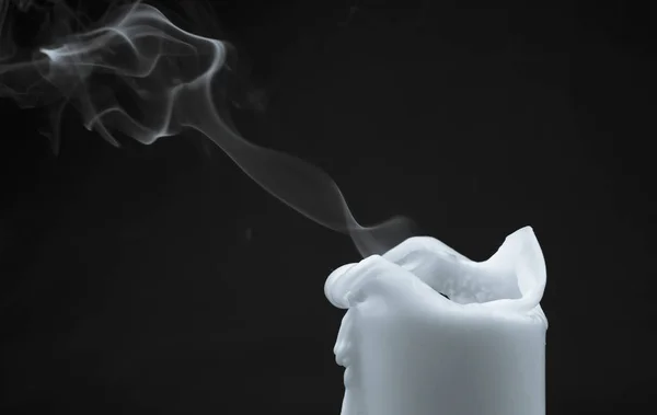 Extinct white candle with smoke on a black background, black and