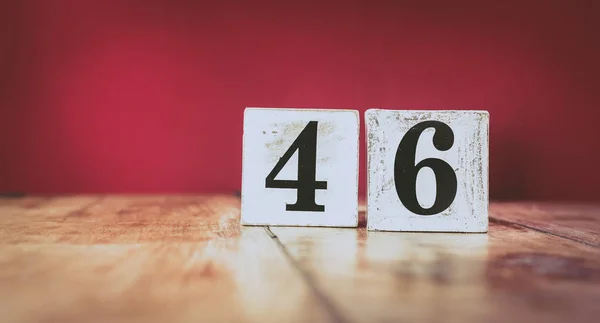 Number 46 on a vintage wooden table and dark maroon background - retro style white blocks