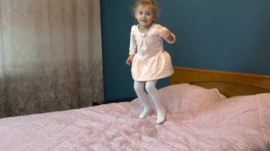 Küçük kız yatakta zıplıyor. Etekli bir çocuk gülümseyip gülüyor. Yavaş çekim