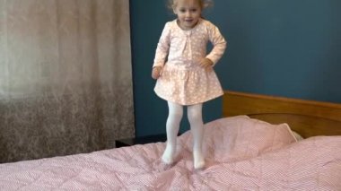 Küçük kız yatakta zıplıyor. Etekli bir çocuk gülümseyip gülüyor. Yavaş çekim