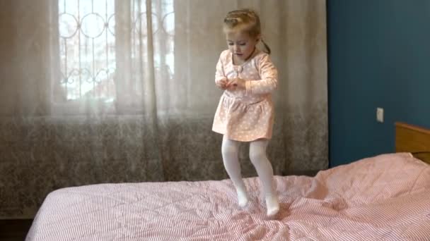 Niña saltando sobre la cama. Un niño con falda sonríe y ríe. Movimiento lento — Vídeo de stock