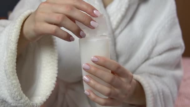 Vrouw sluit het deksel van shampoo. Een vrouw in een badjas houdt een pot reisshampoo vast. Close-up — Stockvideo