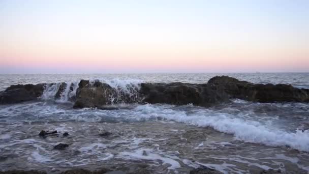 Wellen auf dem Mittelmeer. Wellen schlagen bei rosa Sonnenuntergang auf die Felsen. Zeitlupe — Stockvideo