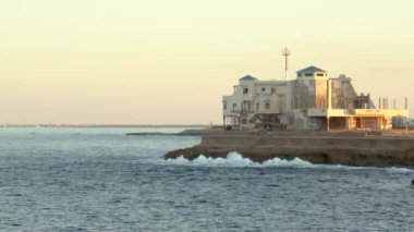 Bir uçurumda Sahil Güvenlik Kalesi. Büyük taş bina. Akdeniz 'in etrafında. Dalgalar kayalara çarpıyor.