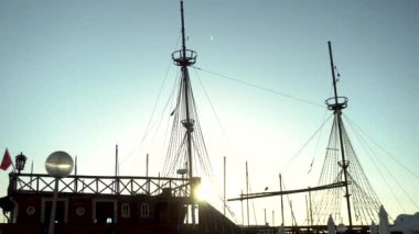 Körfezdeki iskelede bir korsan gemisi duruyor. Eski ahşap gemi. Geminin arkasında bir fil parlıyor. Parılda