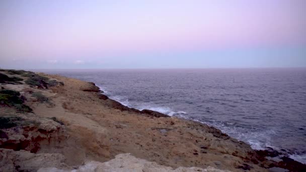 Волны на Средиземном море. Волны ударялись о скалы на скалистом берегу. Розовый закат — стоковое видео