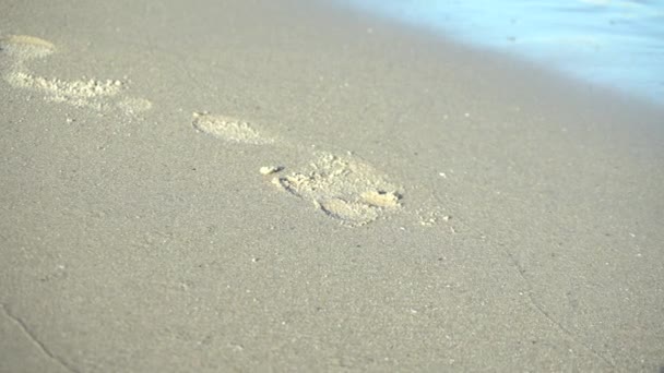 Ślad stopy na piasku. Fala zmywa ślady stóp. Fale docierają do brzegu. — Wideo stockowe